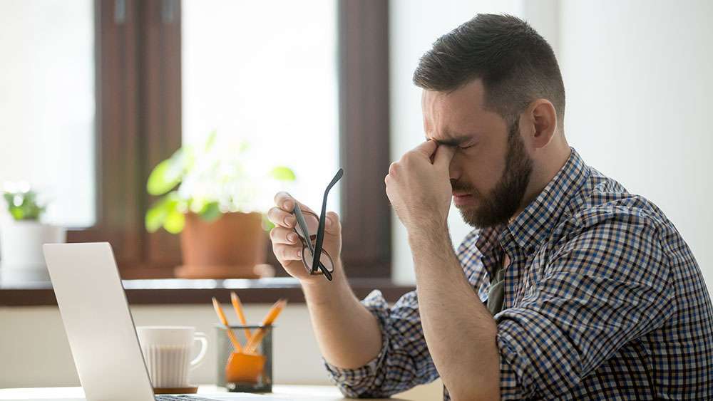 Man holds head while looking at computer