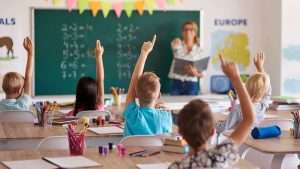 School classroom with students raising hands to answer the teacher's question